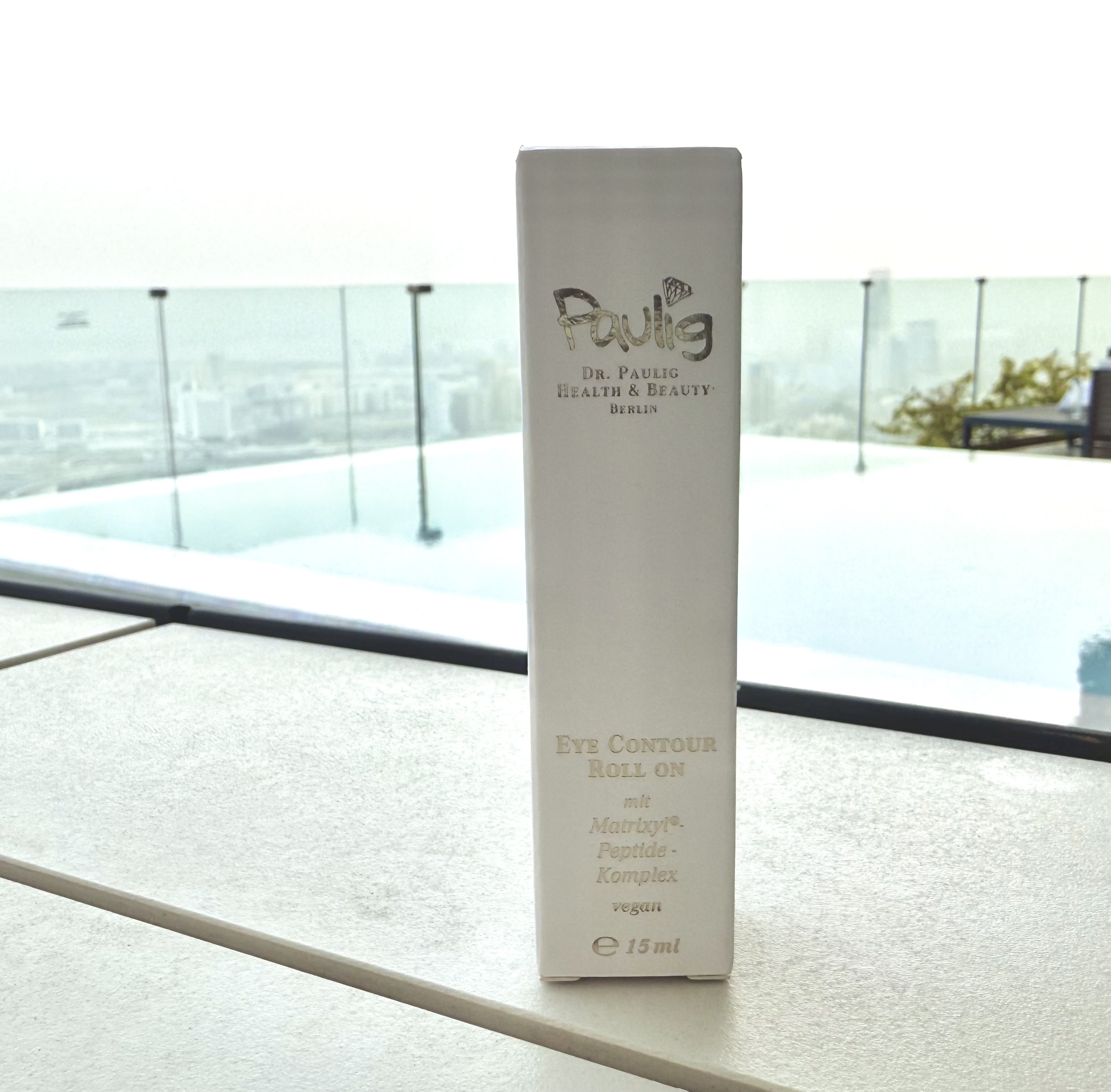 Eine Verpackung für Dr. Paulos Eye Contour Roll-On steht auf einem Tisch mit Poolblick.