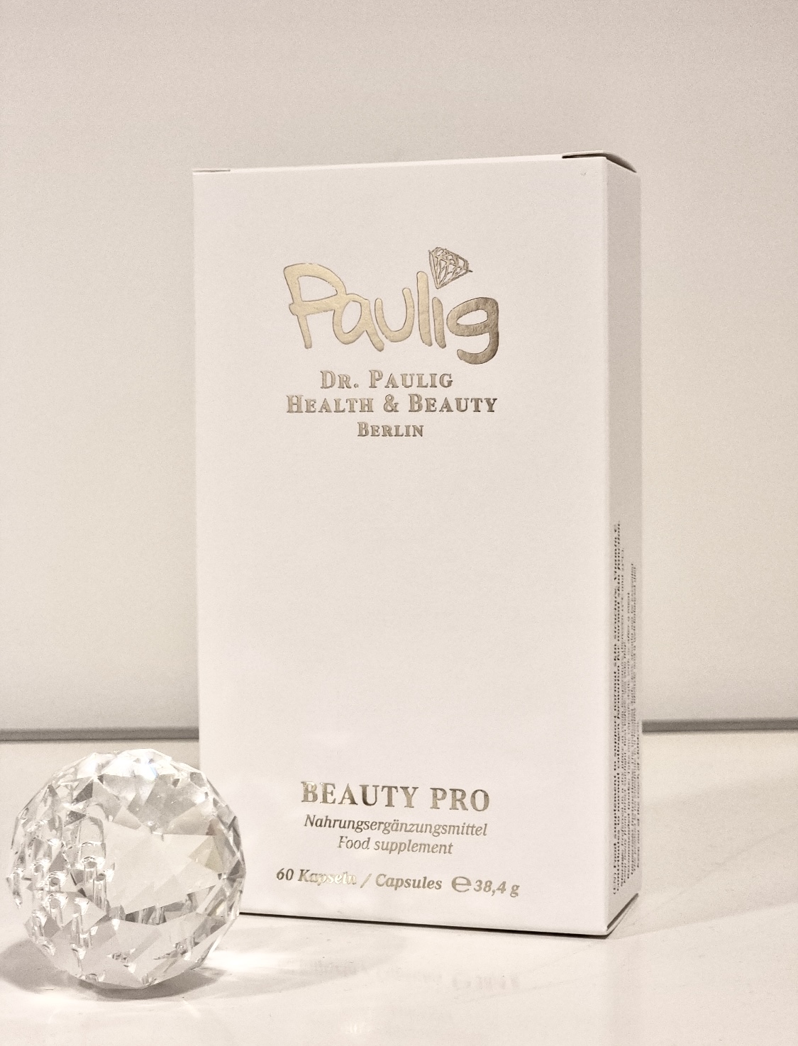 Eine weiße Beauty Pro Verpackung von Dr. Paulig mit goldener Schrift steht neben einem funkelnden Kristall